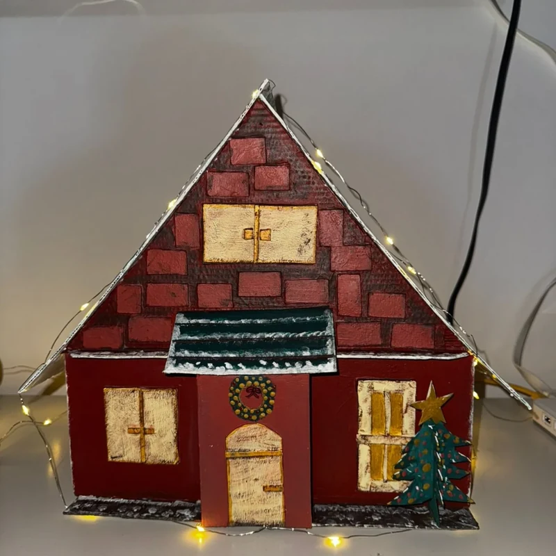 Casinha de tijolinhos vermelhos com guirlanda na porta, pinheirinho de Natal e luzes acesas