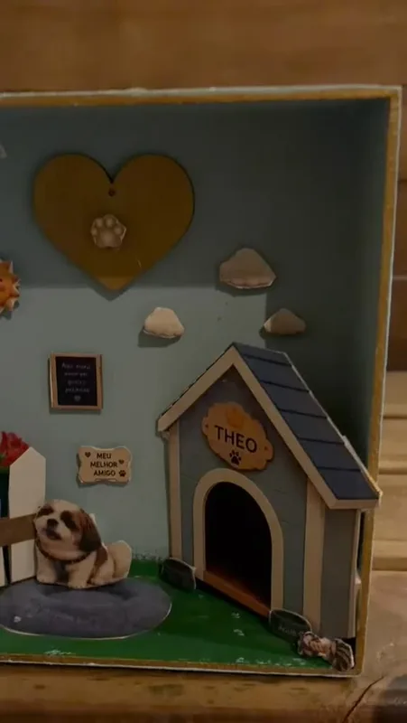 Caixinha com um cachorrinho branco diante da casinha com o nome do pet, coração dourado e nuvens ao fundo